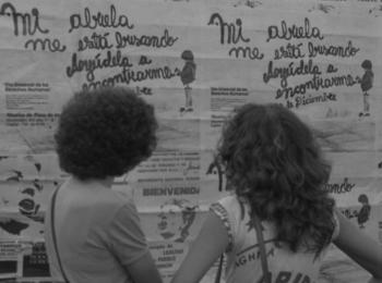La imagen muestra a dos personas mirando un cartel que dice 'Mi abuela me está buscando, ayúdela a encontrarme.', de Abuelas de Plaza de Mayo.